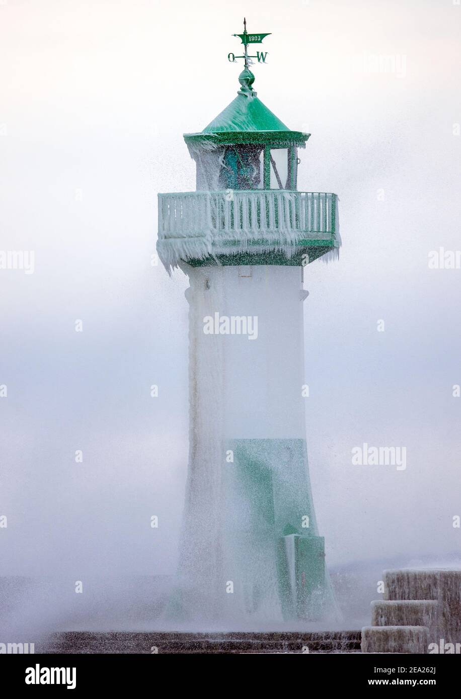 Sassnitz, Deutschland. Februar 2021, 07th. Am teilweise eisigen Leuchtturm am Hafen bricht eine Welle aus. Starke Winde verursachen Schneewehen und Eisbildung an der Küste im Norden der Insel. Der Deutsche Wetterdienst (DWD) erwartet am Wochenende Schneestürme und Permafrost für Norddeutschland. Quelle: Jens BŸttner/dpa-Zentralbild/dpa/Alamy Live News Stockfoto
