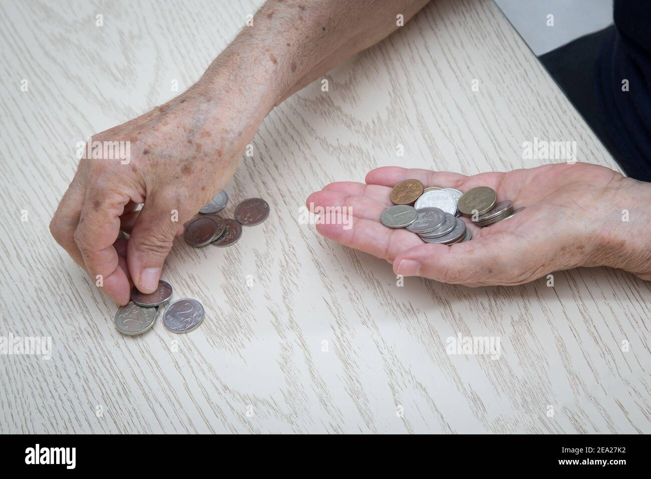 Hände einer alten pensionierten Frau Nahaufnahme auf dem Hintergrund eines hellen Tisches mit einer Kleinigkeit, Eisenmünzen von russischem Geld. Das Konzept der kleinen siz Stockfoto