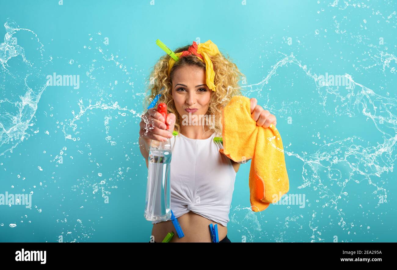 Blonde Hausfrau splashs Desinfektionsmittel, um Viren und Bakterien zu entfernen. Cyanfarbener Hintergrund Stockfoto