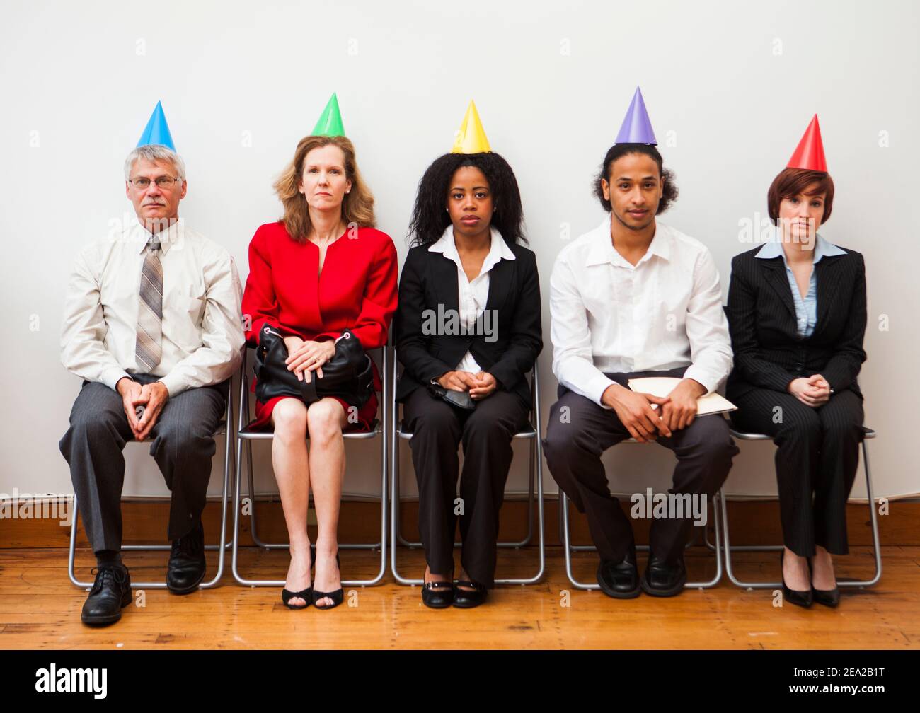 Eine Gruppe von Büroangestellten, die gelangweilt oder desinteressiert aussehen, während sie Partyhüte tragen. Humorvolles Geschäftskonzept. Stockfoto