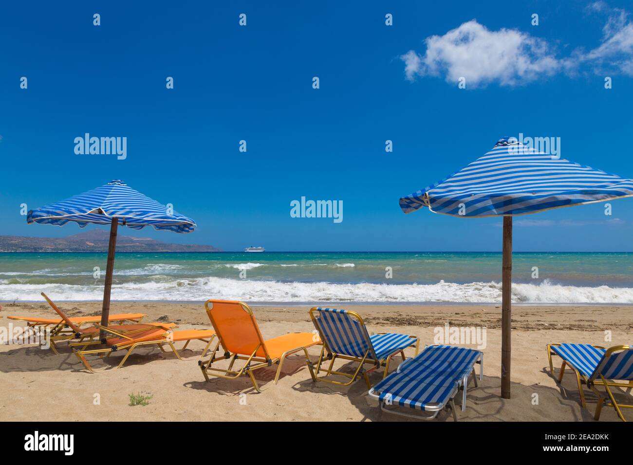 Kreta Strand Kalyves. Blaue und gelbe Sonnenschirme und Sonnenliegen vor der Kulisse eines wunderschönen blauen Meeres an einem sonnigen Tag. Öffentlicher Strand Kalyves auf Kreta Stockfoto