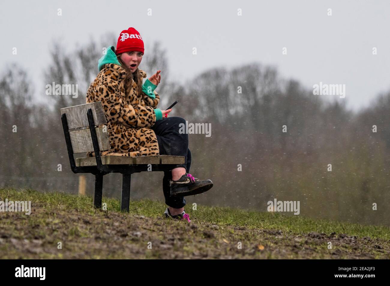 London, Großbritannien. Februar 2021, 7th. Eine Frau in einem Leopardenmuster-Mantel spielt mit ihrem Telefon trotz des leichten Schnees im Gesicht - EIN leichtes staubwischen os Schnee schlingt über einen kalten Parliament Hill. Es ist ziemlich voll, trotz Lockdown 3, wie die Menschen frische Luft und Bewegung suchen. Kredit: Guy Bell/Alamy Live Nachrichten Stockfoto