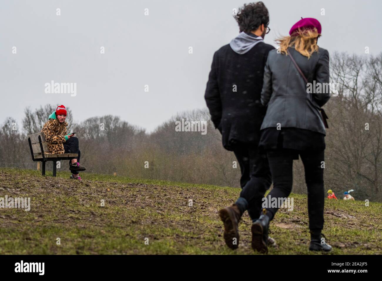 London, Großbritannien. Februar 2021, 7th. Eine Frau in einem Leopardenmuster-Mantel spielt mit ihrem Telefon trotz des leichten Schnees im Gesicht - EIN leichtes staubwischen os Schnee schlingt über einen kalten Parliament Hill. Es ist ziemlich voll, trotz Lockdown 3, wie die Menschen frische Luft und Bewegung suchen. Kredit: Guy Bell/Alamy Live Nachrichten Stockfoto