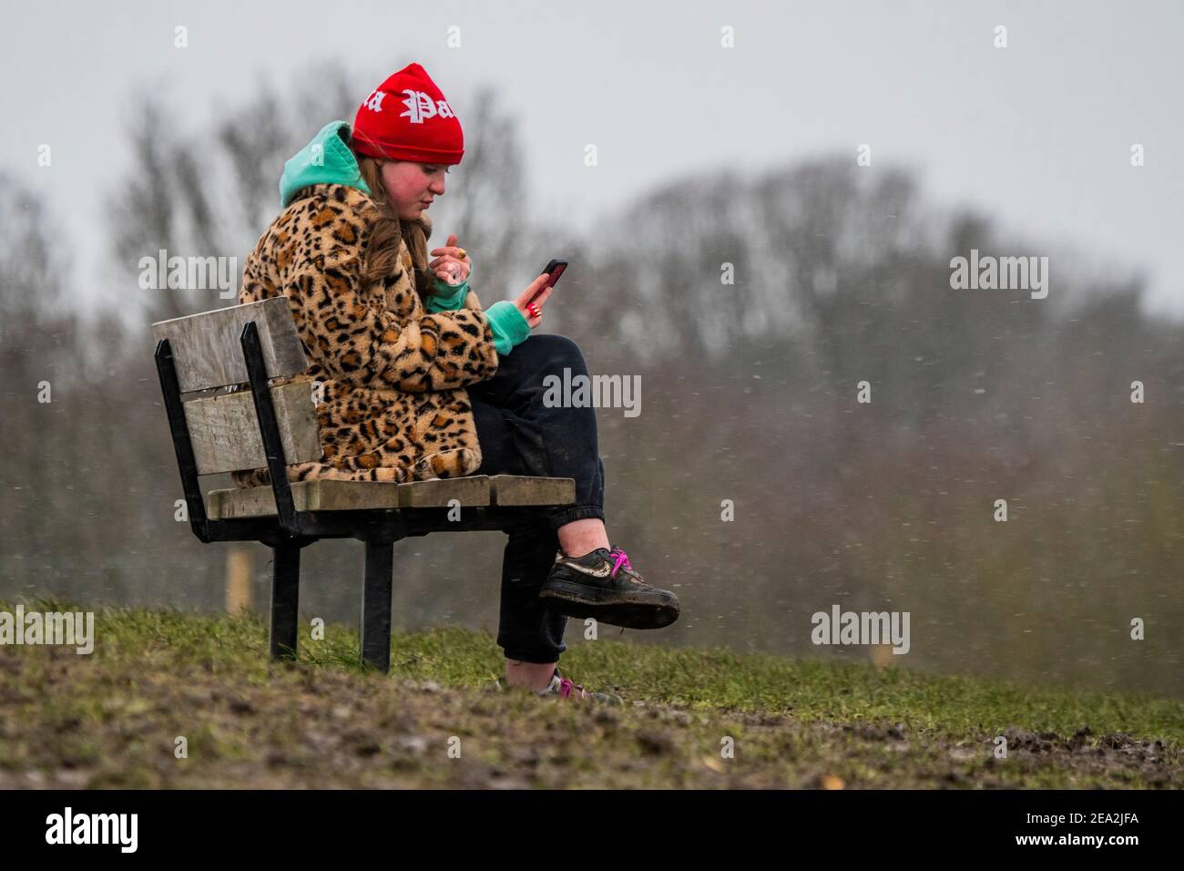 London, Großbritannien. Februar 2021, 7th. Eine Frau in einem Leopardenmuster-Mantel spielt mit ihrem Telefon trotz des leichten Schnees im Gesicht - EIN leichtes staubwischen os Schnee schlingt über einen kalten Parliament Hill. Es ist ziemlich voll, trotz Lockdown 3, wie die Menschen frische Luft und Bewegung suchen. Kredit: Guy Bell/Alamy Live Nachrichten Stockfoto