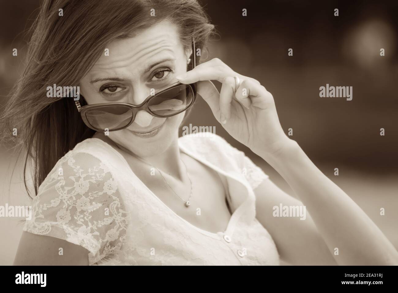 Sepia-Porträt einer jungen kaukasischen Frau, die über eine große Sonnenbrille schaut Stockfoto