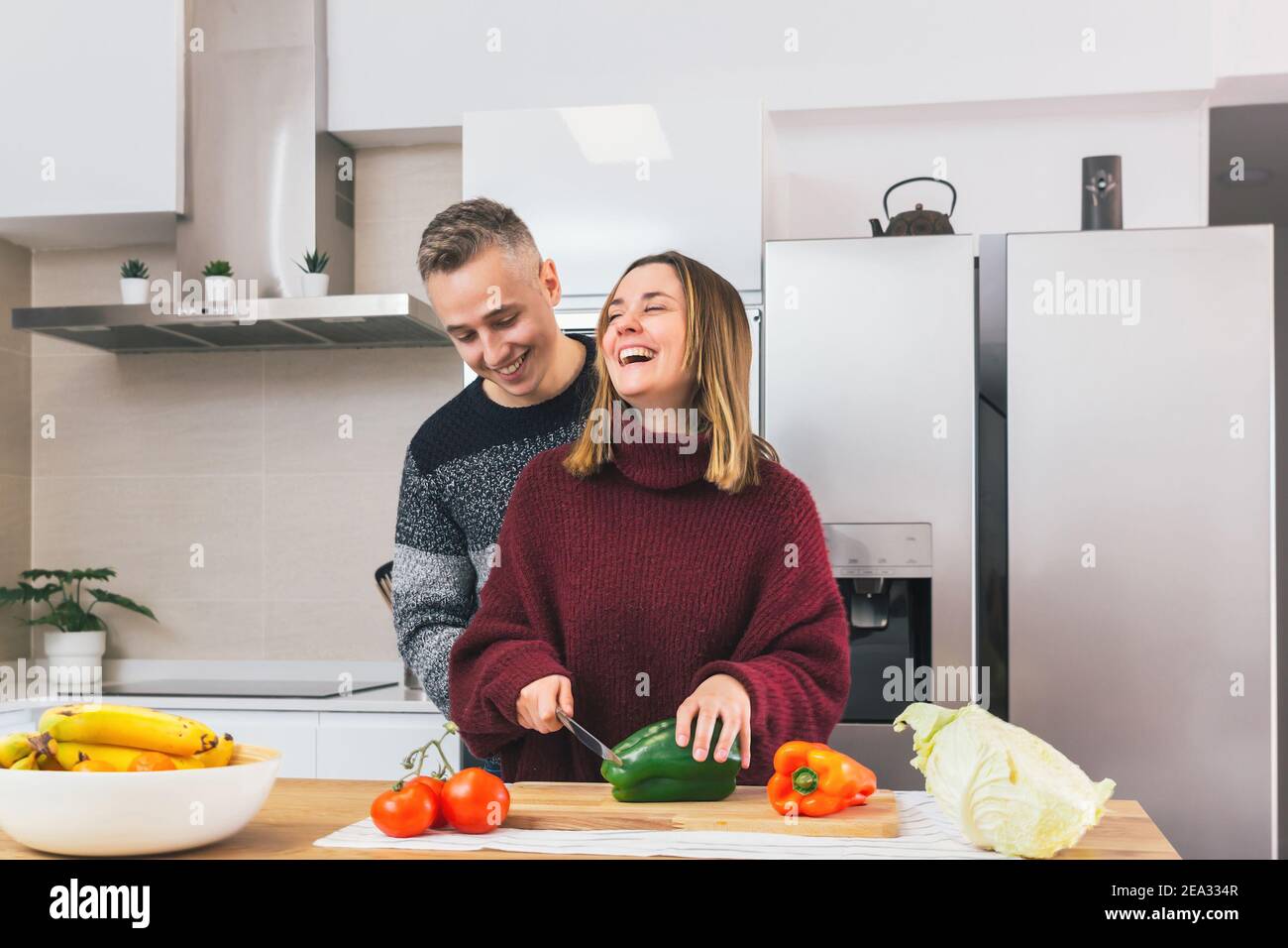 Stock Foto von einem jungen Paar lachen und kochen gesunde Lebensmittel zusammen in der Küche zu Hause. Gemüse für eine vegane Mahlzeit schneiden Stockfoto