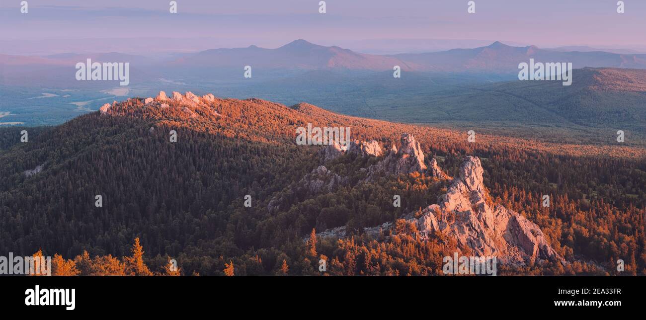 Eine felsige Bergkette mit Wald bedeckt wird durch das rosa Licht der untergehenden Sonne beleuchtet. Ein Naturpark oder Reservat oder Jagdgebiet. Recreati Stockfoto