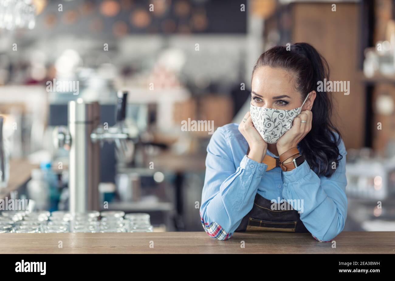 Kellnerin steht in einem Kaffeehaus mit nichts zu tun, trägt Schutzmaske, warten auf Kunden. Stockfoto