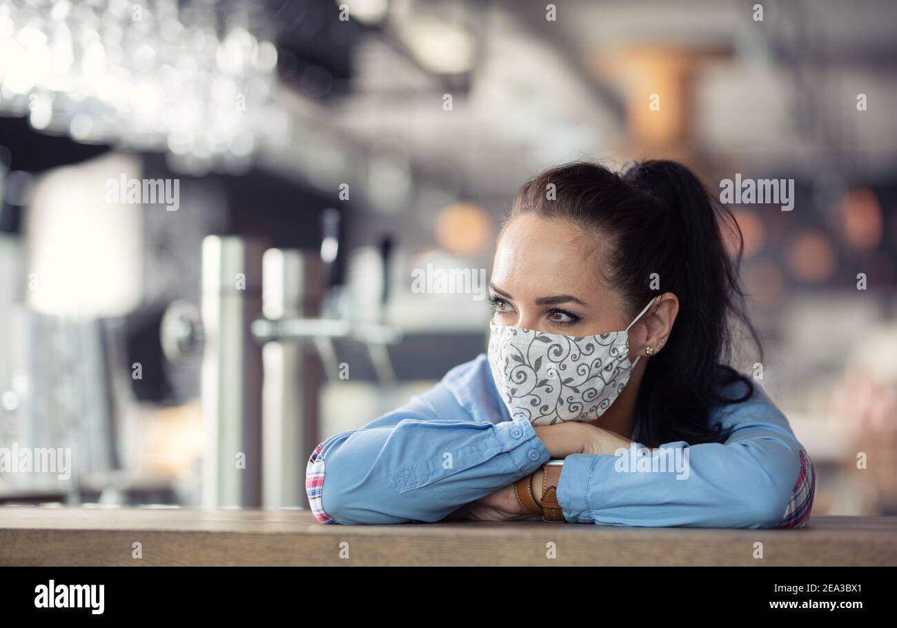 Gesichtsmaske trägt Restaurantbesitzer denkt an die Zukunft ihres Unternehmens lehnt sich an die Bar. Stockfoto