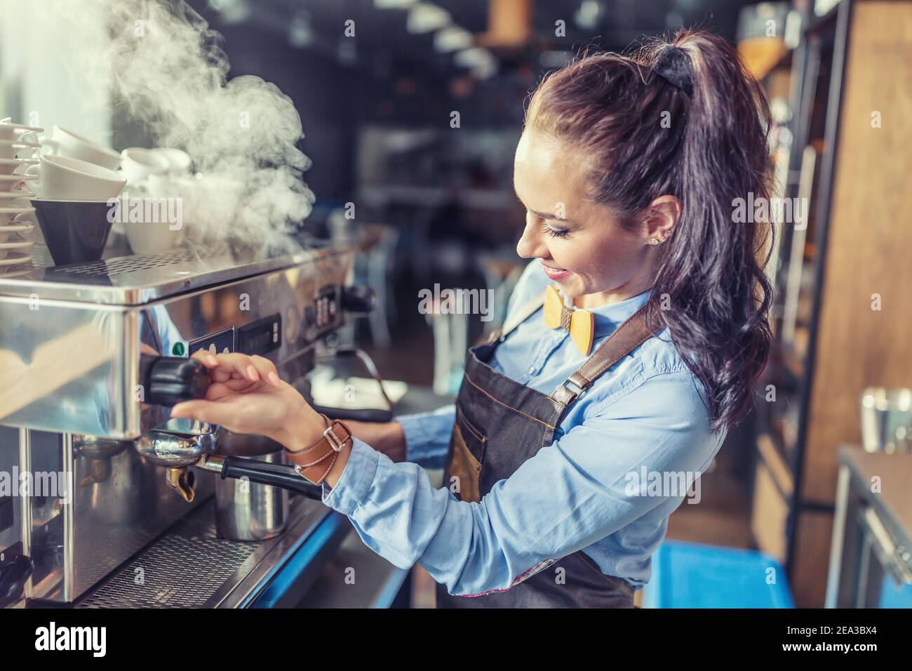 Die professionelle, gut gekleidete Barista dampft in einem Café von der Kaffeemaschine. Stockfoto