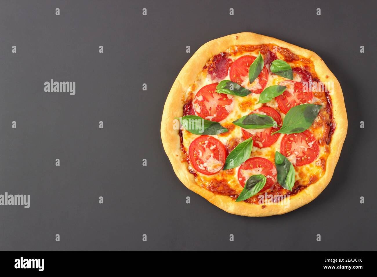 Pizza mit Käse, Wurst, Tomaten und Basilikumblättern isoliert auf schwarzem Hintergrund. Blick von oben Stockfoto
