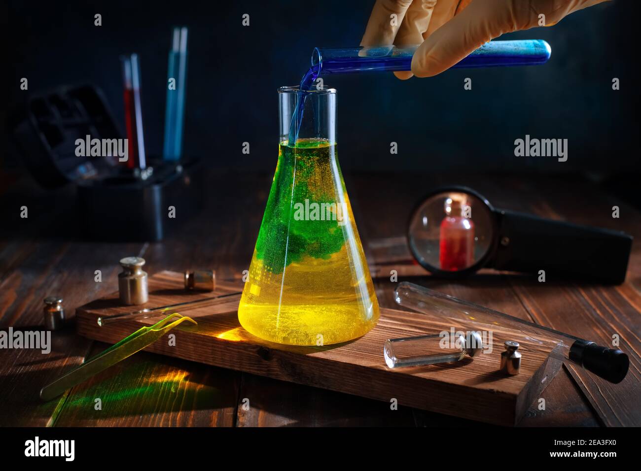 Wissenschaftler gießt blaue Flüssigkeit in gelb in einem chemischen Kolben. Farbwechsel. Wissenschaft, Experimente Stockfoto