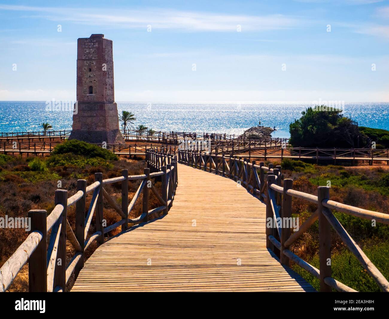 Holzweg zu einem steinernen Wachturm vor den Stränden von Marbella an einem sonnigen Herbsttag. Stockfoto