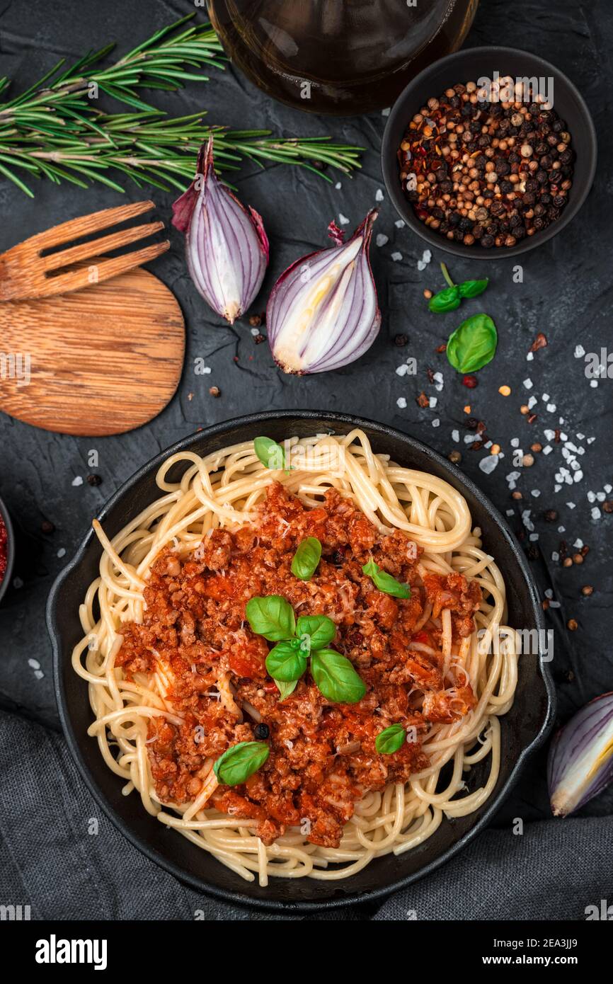 Pasta mit Hackfleisch und Tomatensauce bestreut mit Basilikum auf schwarzem Betonboden. Stockfoto