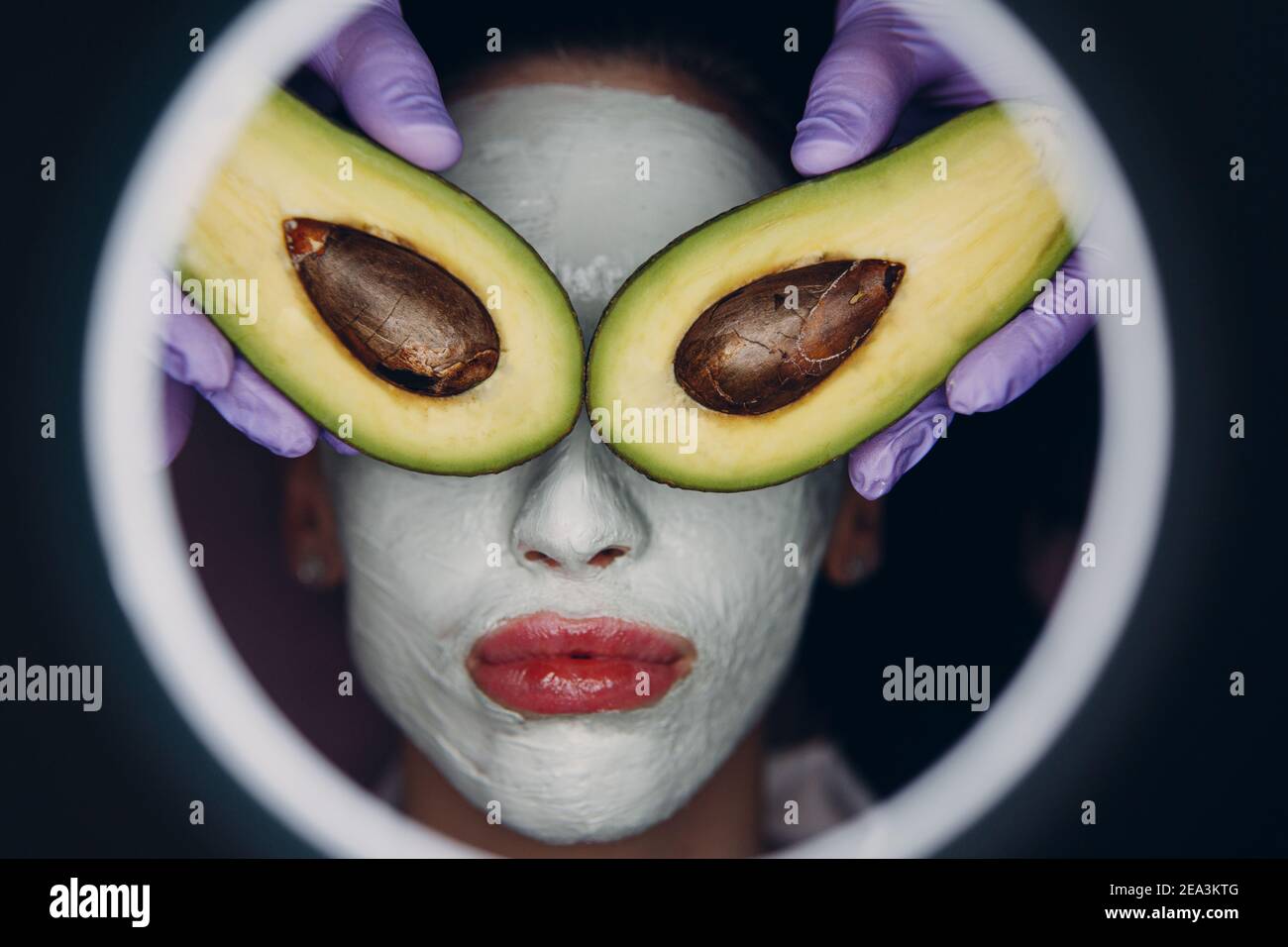 Junge schöne Frau erhalten Gesichts Tonmaske mit Avocado auf ihren Augen in Spa Schönheitssalon. Stockfoto