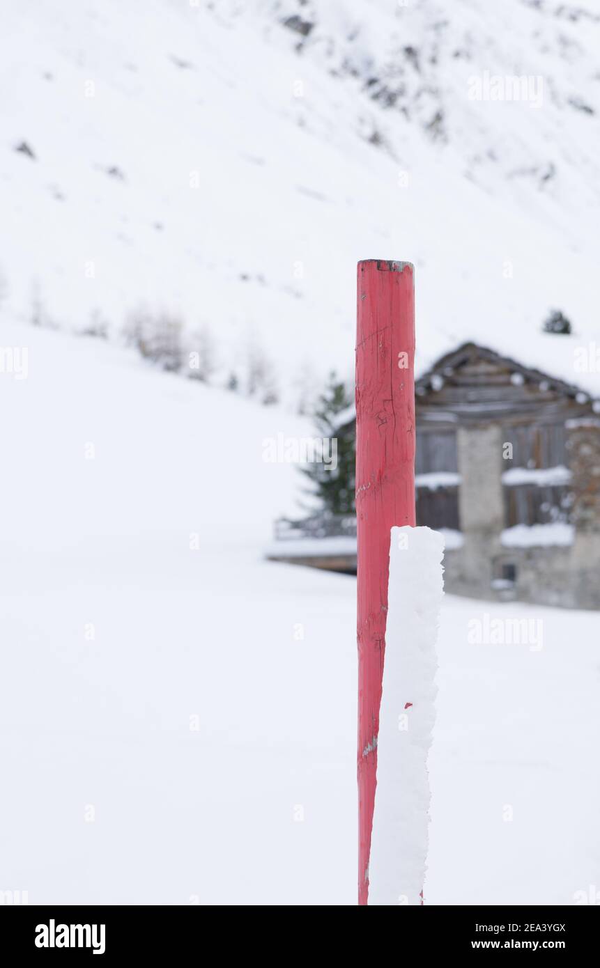 Eine Nahaufnahme eines roten Holzmastes Legen Sie in Schnee und das Holzhaus im Hintergrund Stockfoto