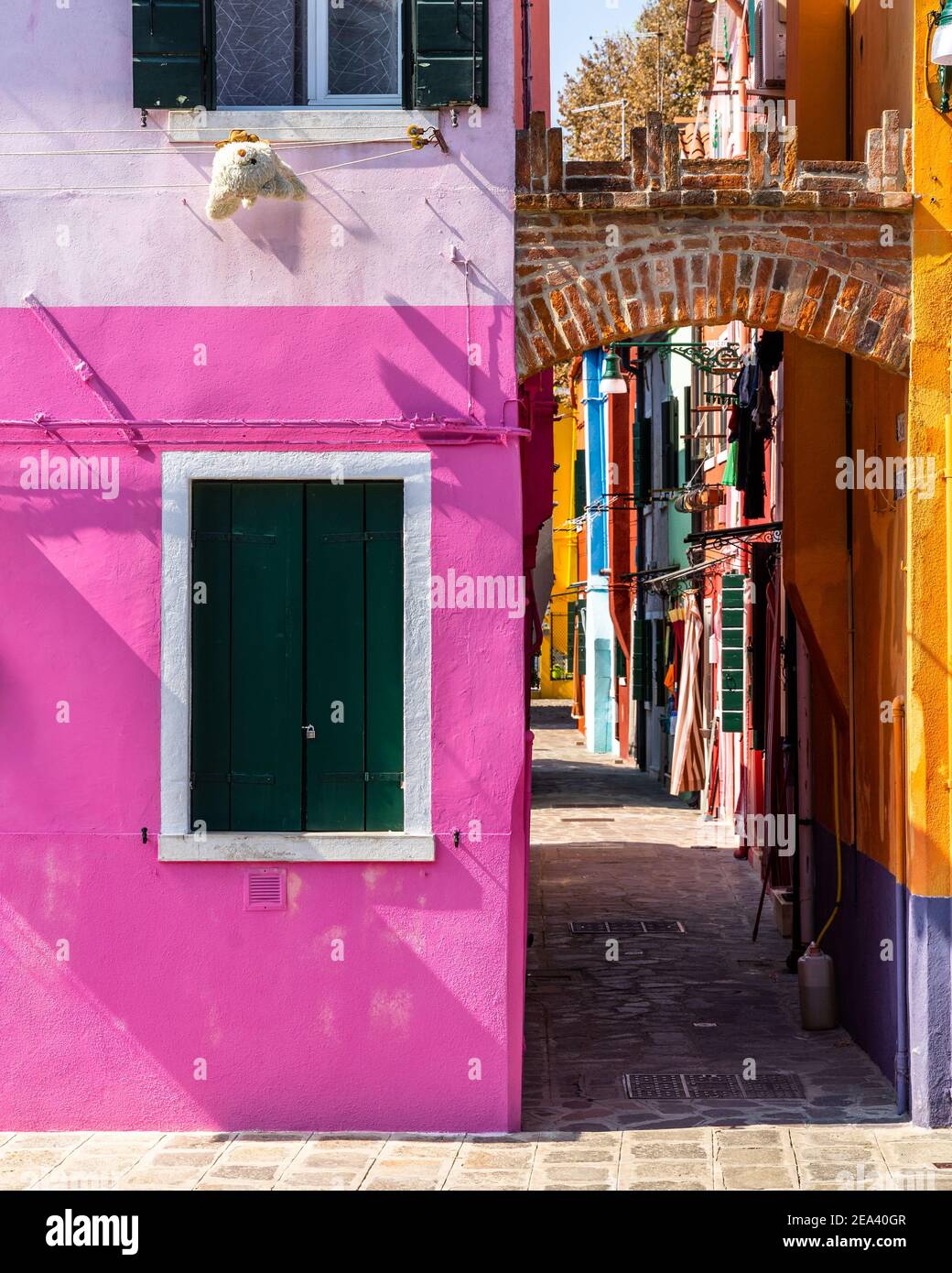 Außenansicht eines leuchtend rosa bemalten Hauses in Burano in der Nähe einer bunten Gasse, Italien Stockfoto
