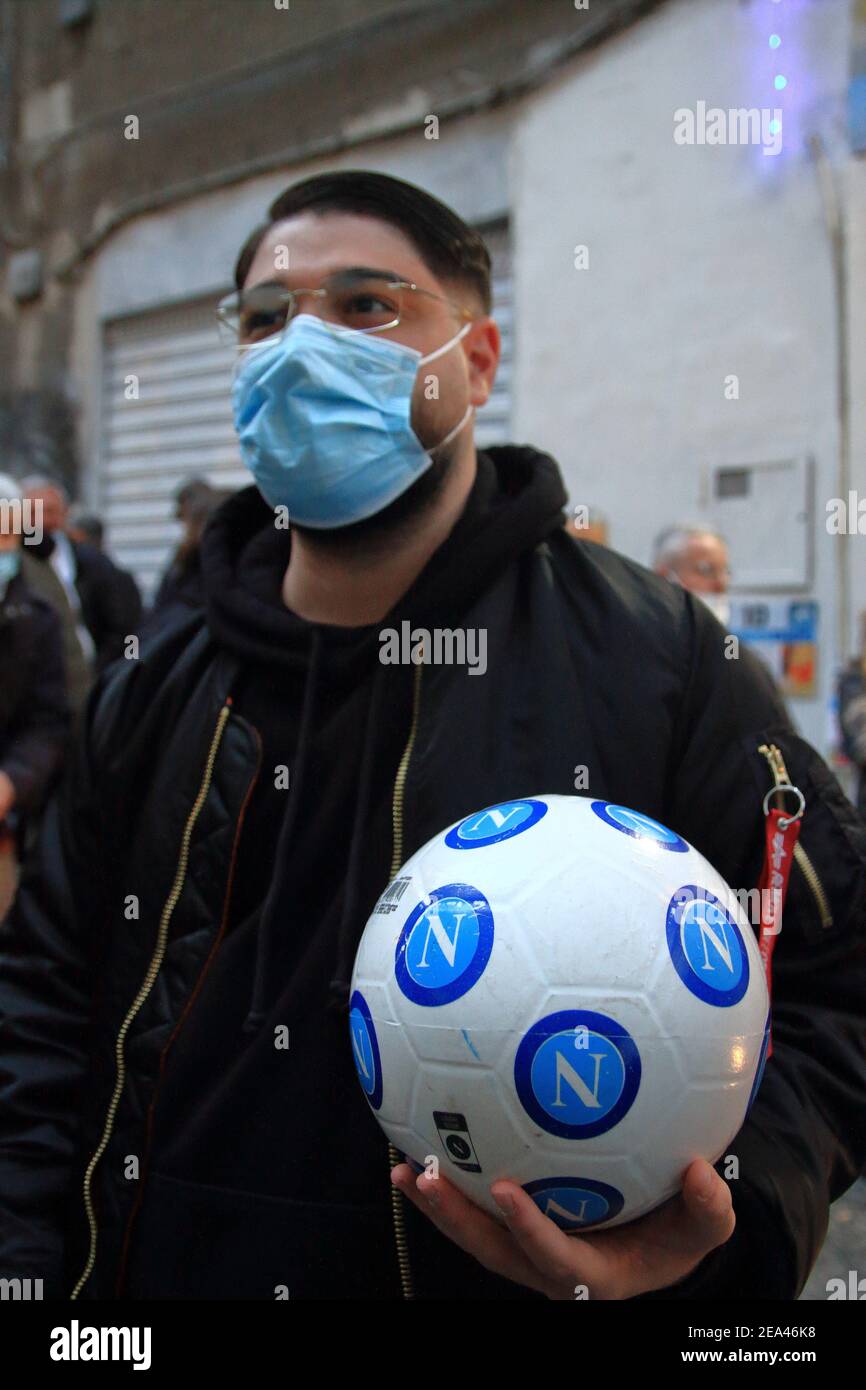 Ein junger Napoli-Fan mit Maske hält in der Hand einen offiziellen Ball der napolischen Fußballmannschaft und sieht sich die Bilder von Diego an den Wänden ausgesetzt. Stockfoto