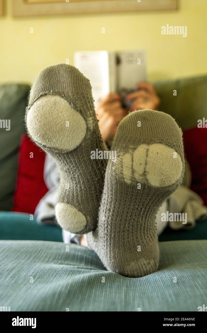 Eine vertikale Aufnahme einer Person, die mit ein Buch liest Alte Socken mit Löchern Stockfoto