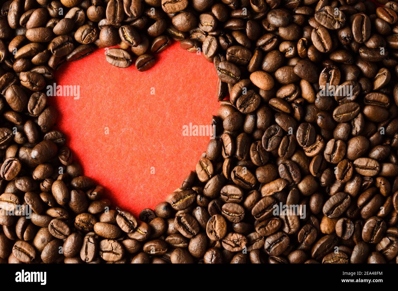 Geröstete Kaffeebohnen auf einem roten strukturierten Hintergrund in Form eines Herzens. Stockfoto