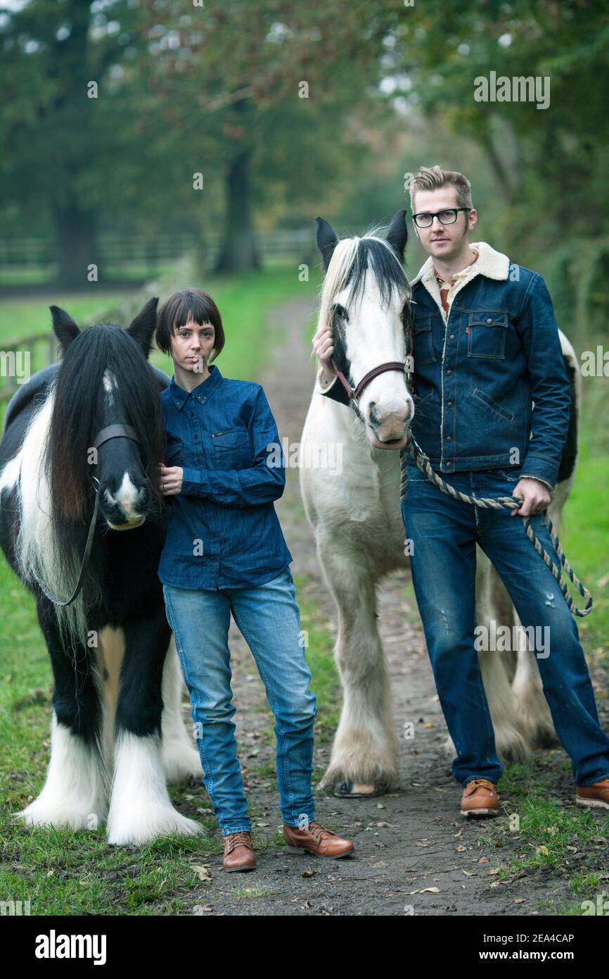 Junges Paar in Jeans Vorbereitung ihrer Pferde für einen Ausritt auf einem ländlichen Bauernhof. Stockfoto