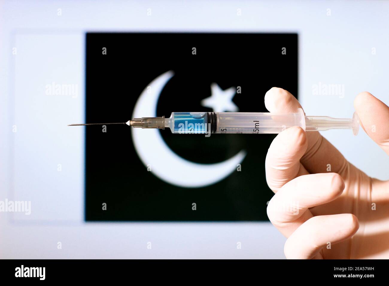 Hand in der Chirurgie Handschuh hält Spritze mit covid Impfstoff. Pakistanische Flagge im Hintergrund Stockfoto