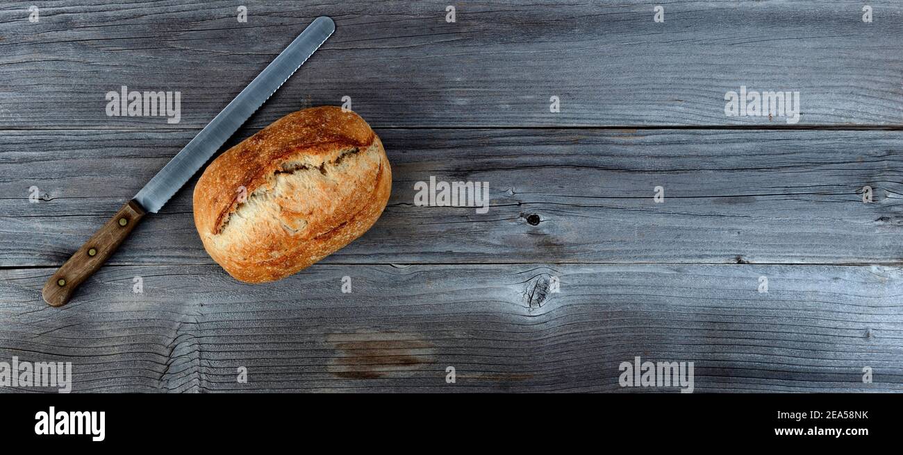 Draufsicht auf hausgemachten vollen Sauerteig Laib Brot mit Schneidmesser auf verwitterten Holzplanken Stockfoto