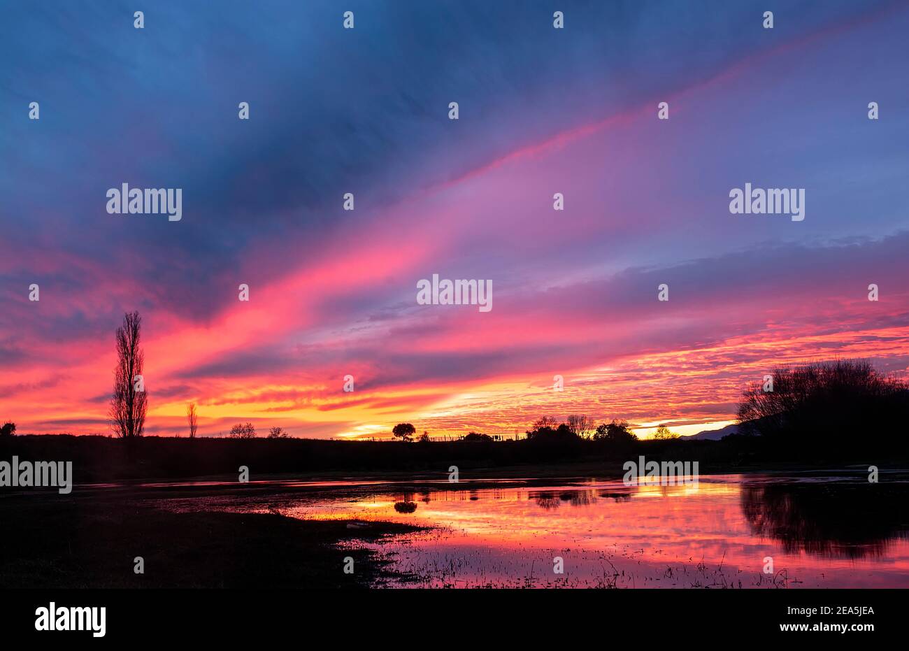 Sonnenuntergang am Flussufer, warme Farben mit Spiegelung Stockfoto