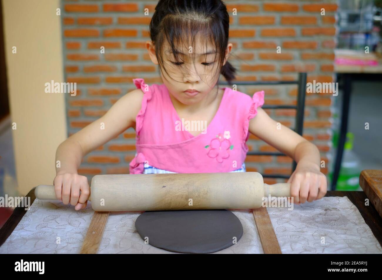 Ein süßes junges asiatisches Mädchen, das in ihrer Töpferklasse Ton Formen lernt, den Ton in ein Gericht formt und verschönt. Stockfoto