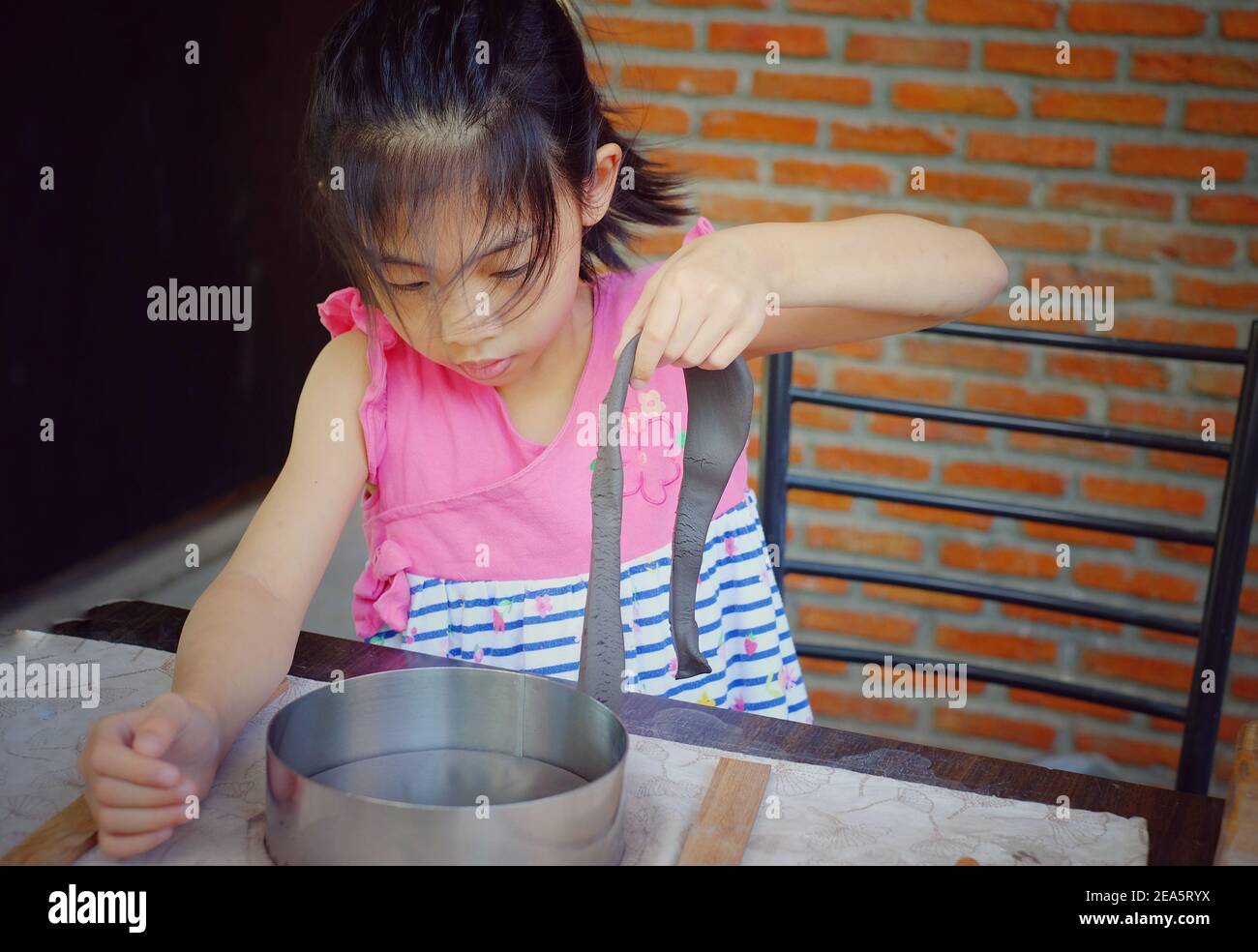 Ein süßes junges asiatisches Mädchen in ihrer Töpferklasse schneidet und formt ihren Ton in eine Schüssel. Stockfoto