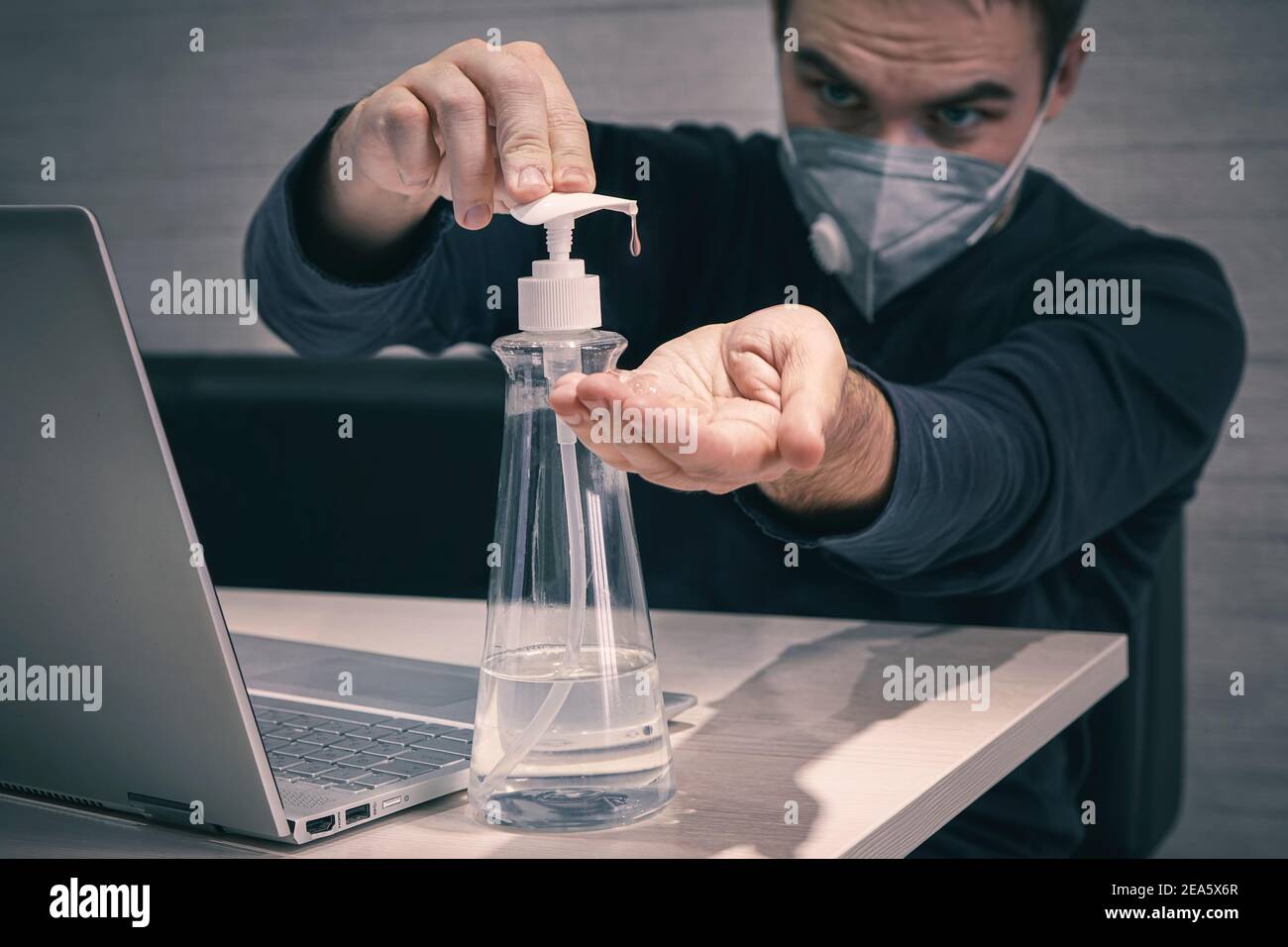Ein junger Arbeiter in einer medizinischen Maske arbeitet von zu Hause in den frühen Morgen. Pandemie covid 19 Coronavirus. Mann behandelt seine Hände mit einem Desinfektionsmittel zu disi Stockfoto