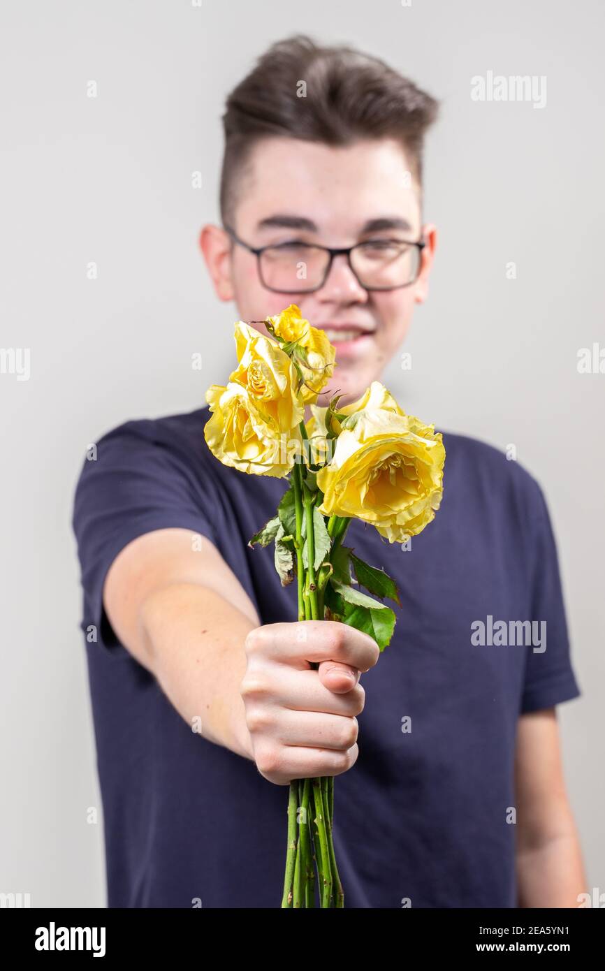 Ein hochmütiger junger Mann hält einen Strauß verwelkter gelber Rosen aus und zeigt ein Feigentrennungskonzept Stockfoto