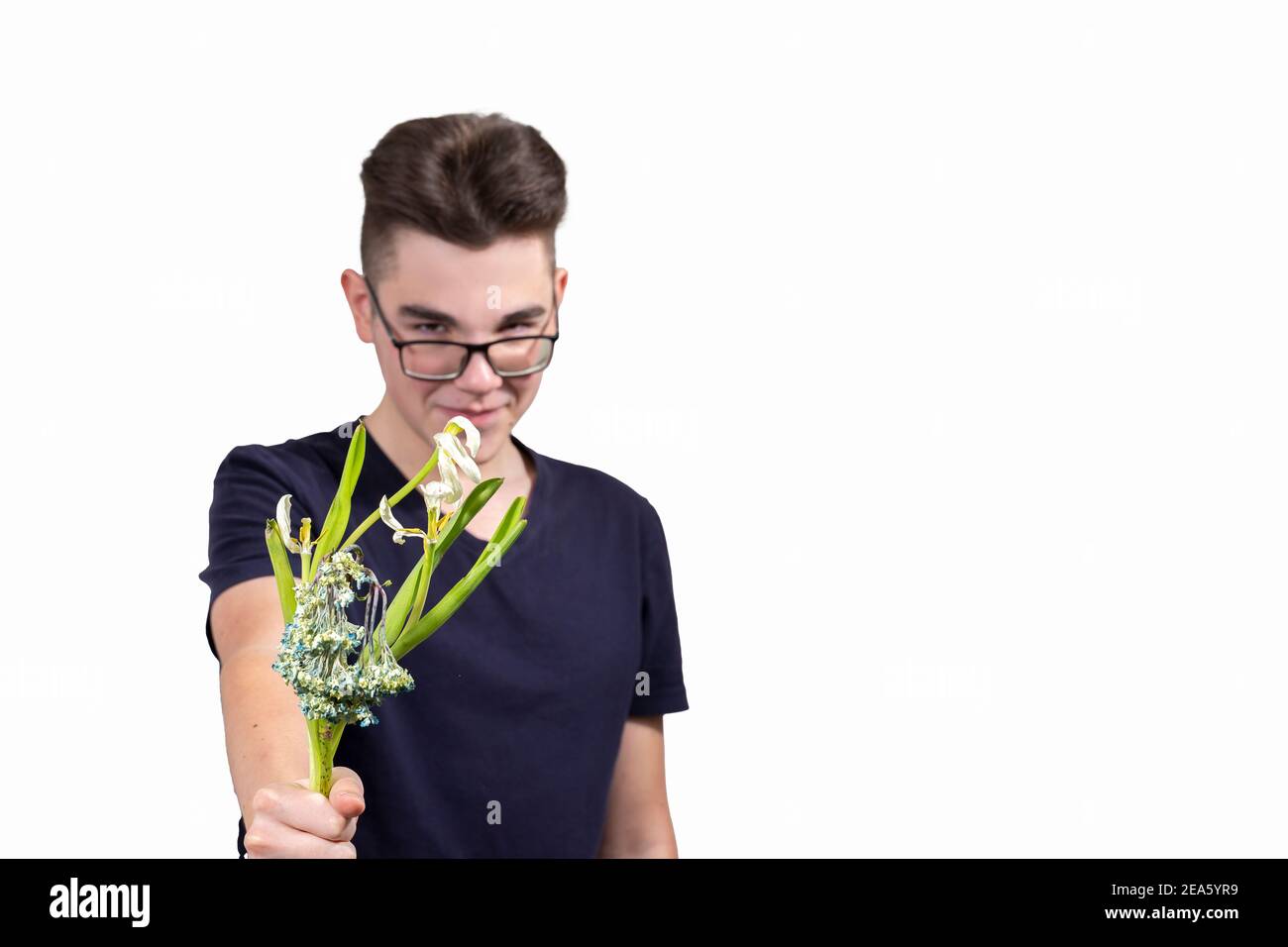 Ein bösartiger junger Mann mit Brille hält einen Strauß von verwelkt Blumen und lächelt. Das Konzept der Gier und Geiz. Konzentrieren Sie sich auf Blumen, Kerl in blu Stockfoto