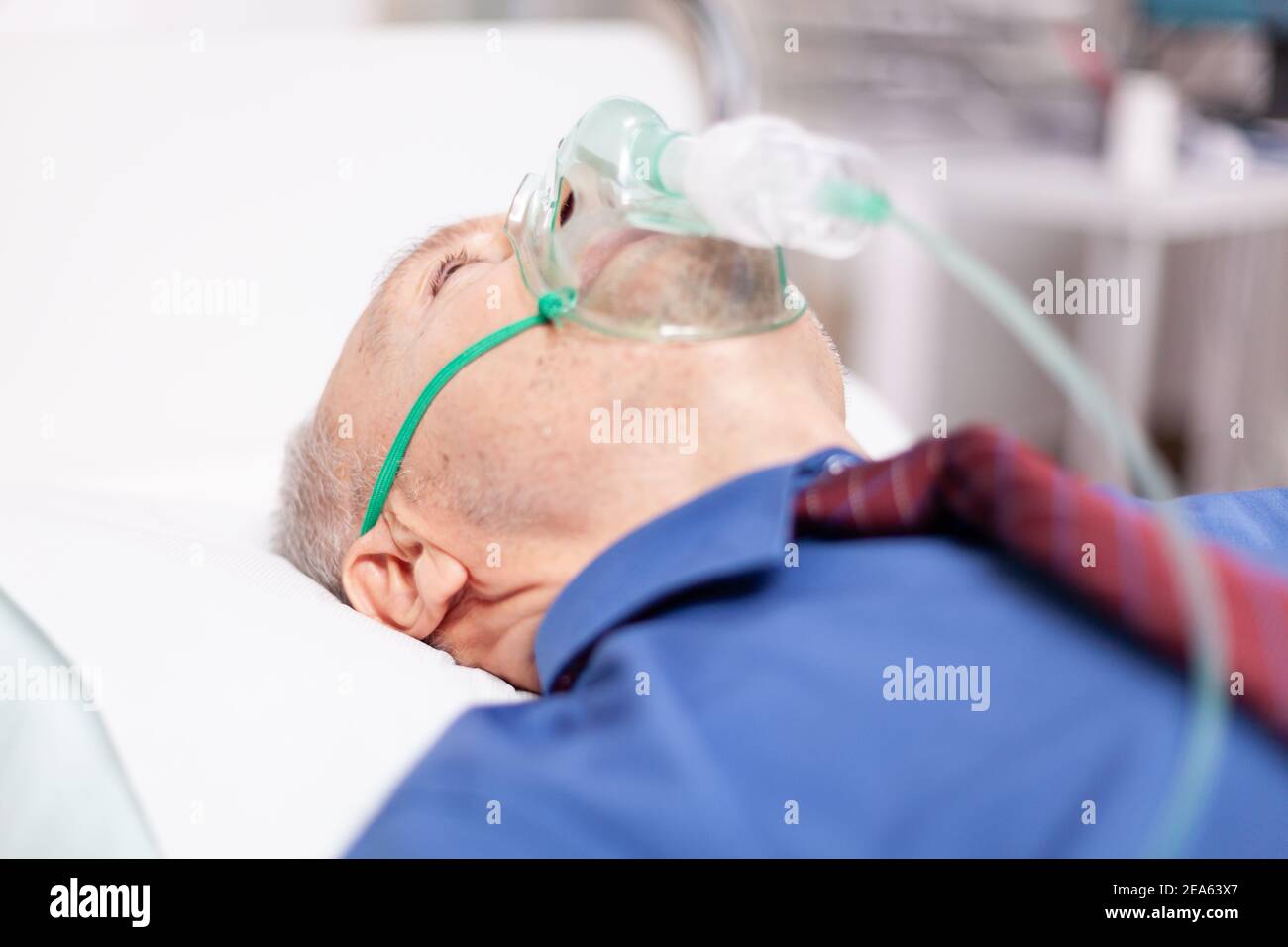 Älterer Mann erhält Behandlung für Lungen, die mit covid19 angesteckt werden, trägt Sauerstoffmaske. Patient im Krankenhauszimmer, der während einer Coronavirus-Pandemie auf einem medizinischen Bett mit infizierter Lunge liegt und ein Atemproblem hat. Stockfoto