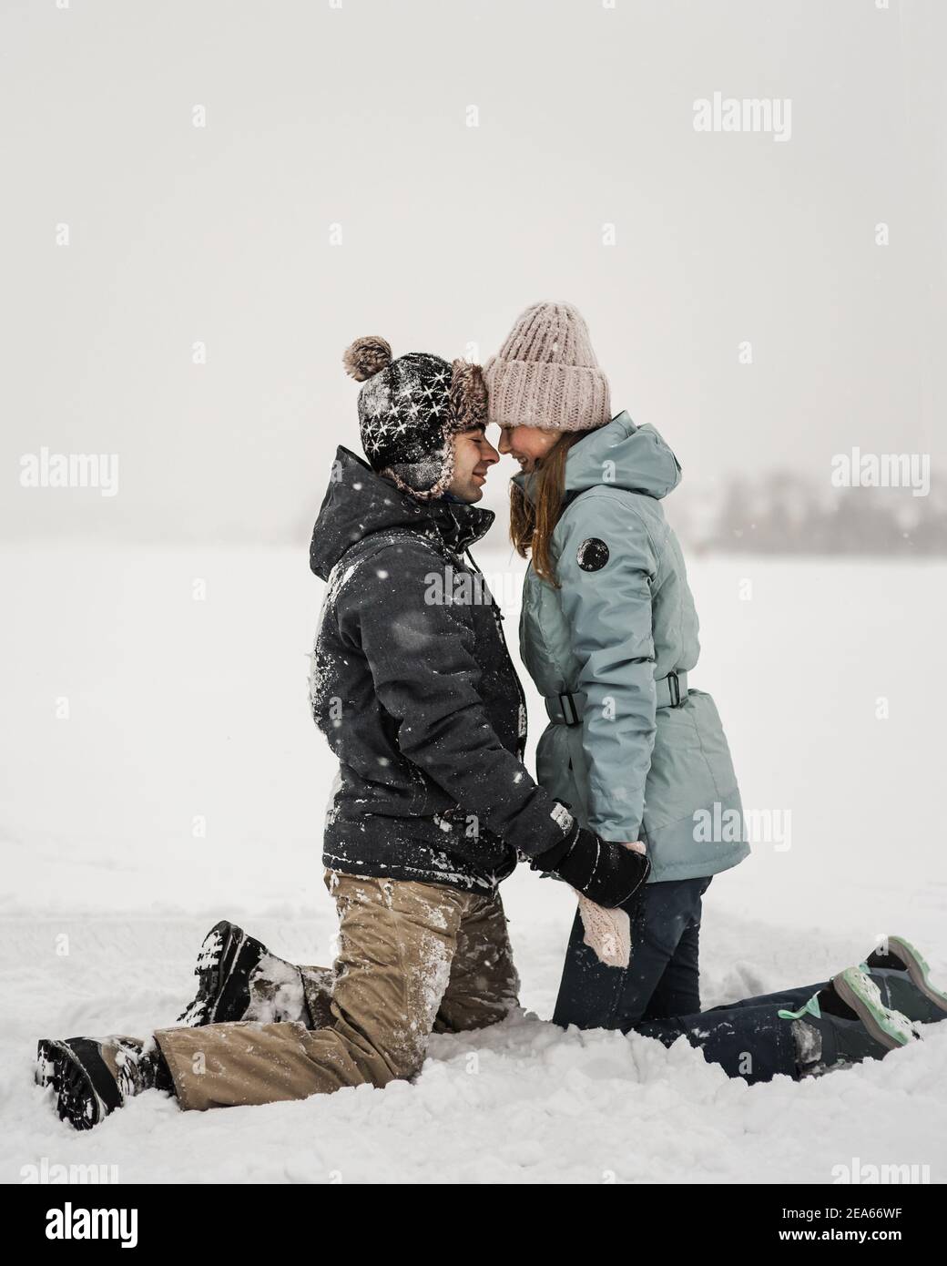 Portrait eines lächelnden verliebten Paares sitzen im Schnee. Junge glückliches Paar zu Fuß im Wintertag Stockfoto
