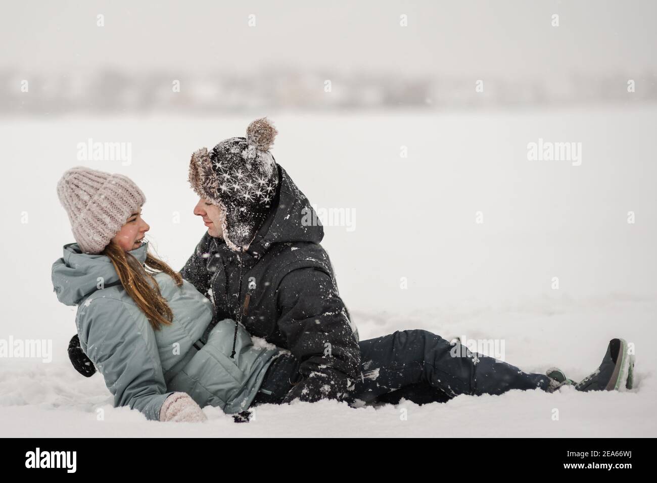 Liebevoller Kerl und Mädchen liegen im Schnee. Junge glückliches Paar zu Fuß im Wintertag Stockfoto