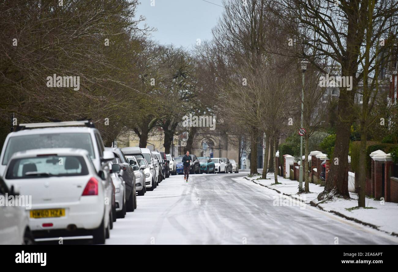 Brighton UK 8th February 2021 - EIN Läufer stampft die verschneiten Straßen rund um den Queens Park in Brighton nach einem leichten Schneefall über Nacht mit weiteren Prognosen für Teile des Ostens und Südostens heute: Credit Simon Dack / Alamy Live News Stockfoto