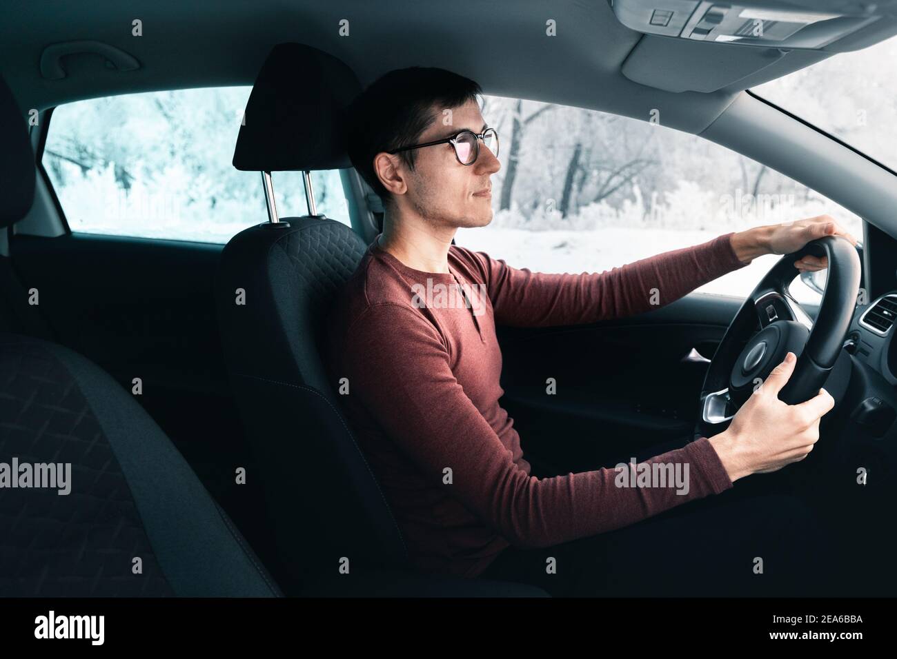Im Winter fährt ein junger Kaukasusmann in stilvoller Brille auf einer Landstraße. Das Konzept der Autovermietung und Reisen Stockfoto