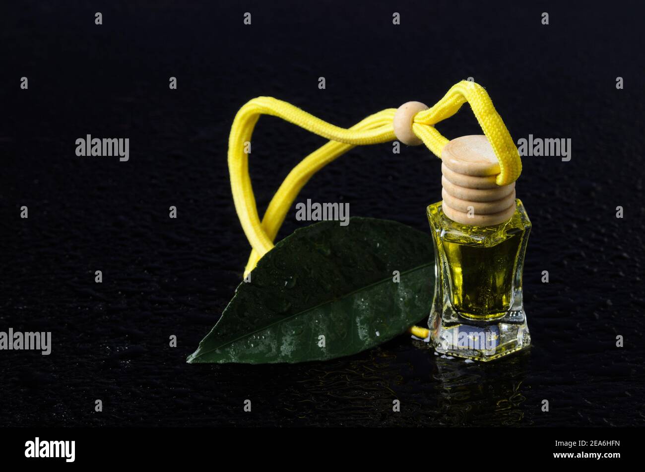 Eine Flasche gelber Flüssigkeit mit einem Holzstopfen und einem grünen Blatt Zitronenbaum mit Wassertröpfchen auf einem schwarzen Holzhintergrund. Aromatische Öle. Selektiv Stockfoto