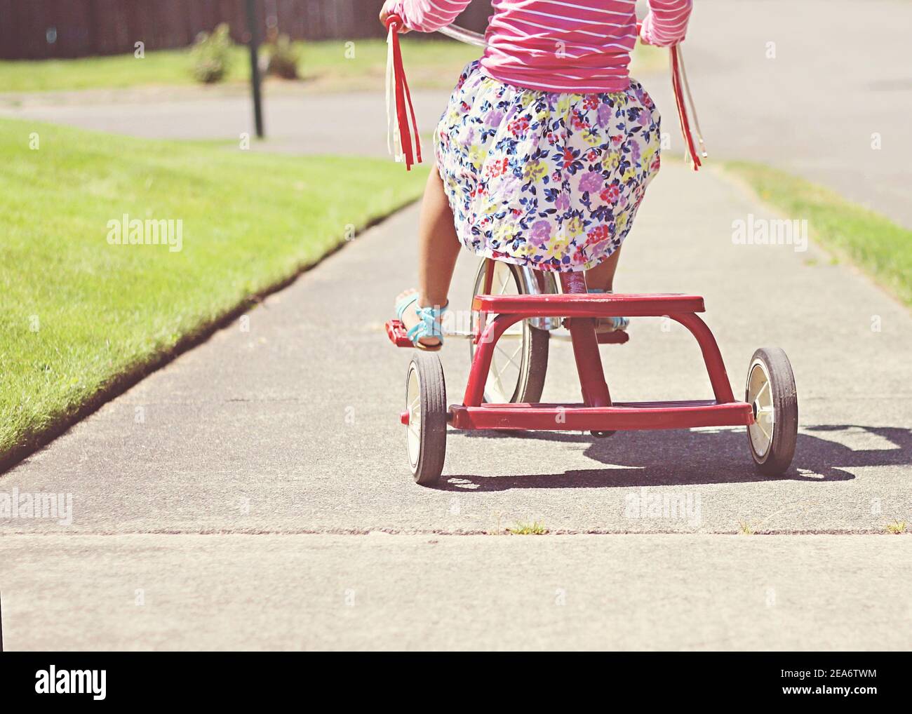 Rückansicht eines Mädchens, das auf einem Dreirad auf dem Bürgersteig, Washington, USA, radelt Stockfoto