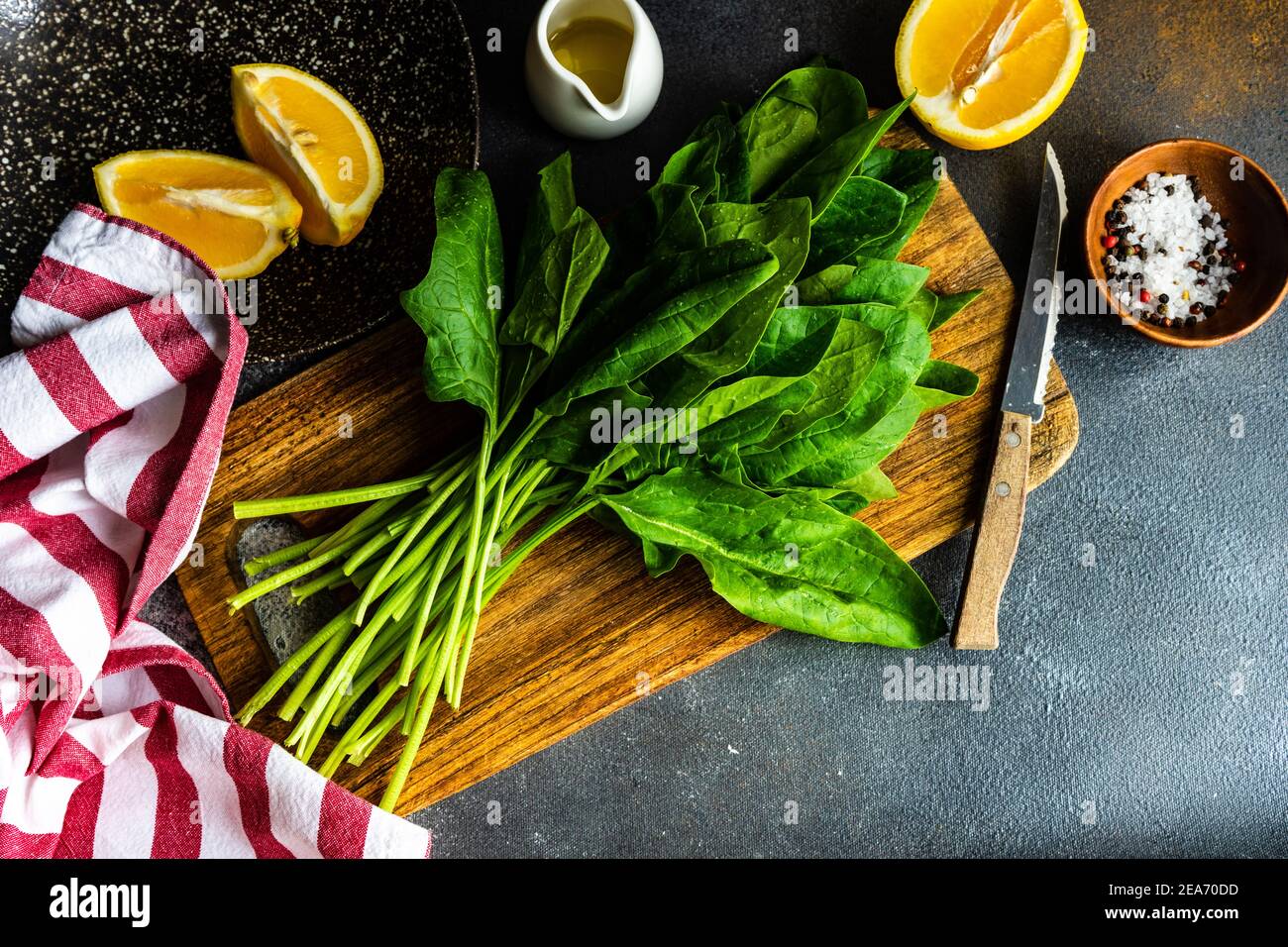 Frische Spinatblätter auf einem Schneidebrett neben Orangen, Olivenöl und Salz und Pfeffer Stockfoto