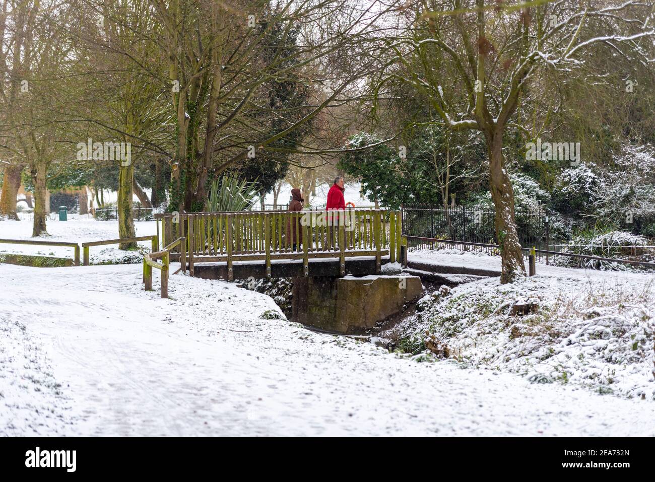 Southend on Sea, Essex, Großbritannien. Februar 2021, 8th. Der Schnee von Storm Darcy ist gefroren und hat die Bedingungen tückisch gemacht. Im Priorat Park der Stadt trainieren die Menschen. Menschen, die eine Brücke über einen Bach überqueren Stockfoto