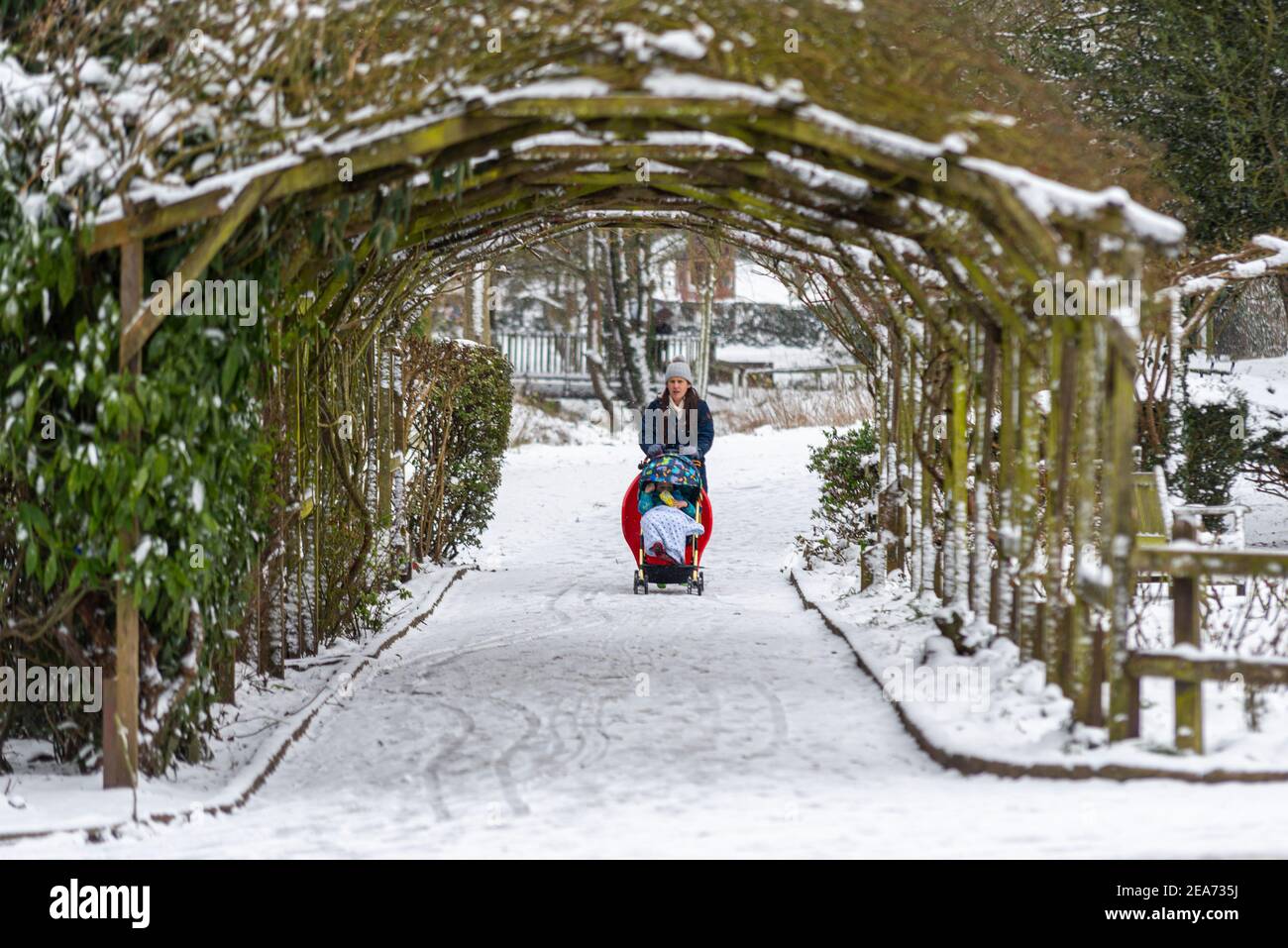 Southend on Sea, Essex, Großbritannien. Februar 2021, 8th. Der Schnee von Storm Darcy ist gefroren und hat die Bedingungen tückisch gemacht. Im Priorat Park der Stadt trainieren die Menschen. Eine Mutter schob ein Kind unter eine Pergola Stockfoto