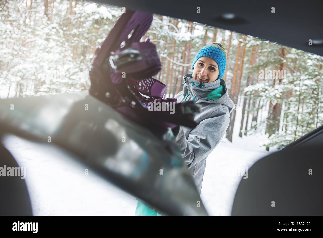 Glückliche junge Frau legte das Snowboard in den Kofferraum. Winterurlaub Stockfoto