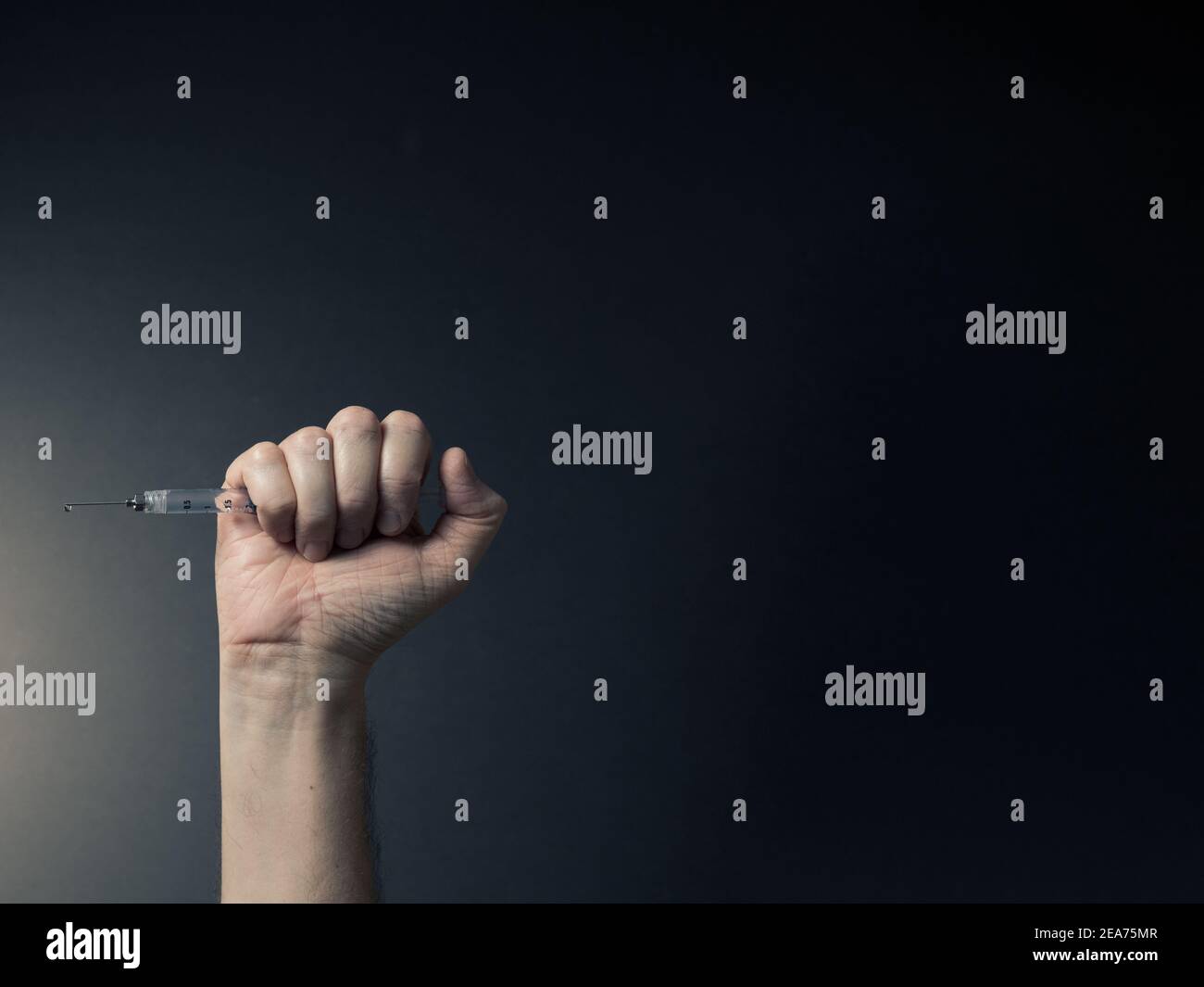 Farbbild von Mann geballte Hand halten Spritze horizontal mit Flüssigkeitstropfen auf Nadelspitze, mit dramatischen Beleuchtung und Text Raum nach rechts Stockfoto