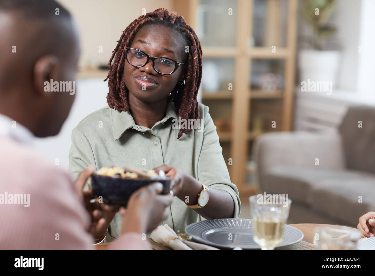 Portrait eines modernen afroamerikanischen Paares, das zu Hause gemeinsam zu Abend essen kann, Fokus auf lächelnde junge Frau, die mit ihrem Mann zusammen essen kann, Kopierraum Stockfoto
