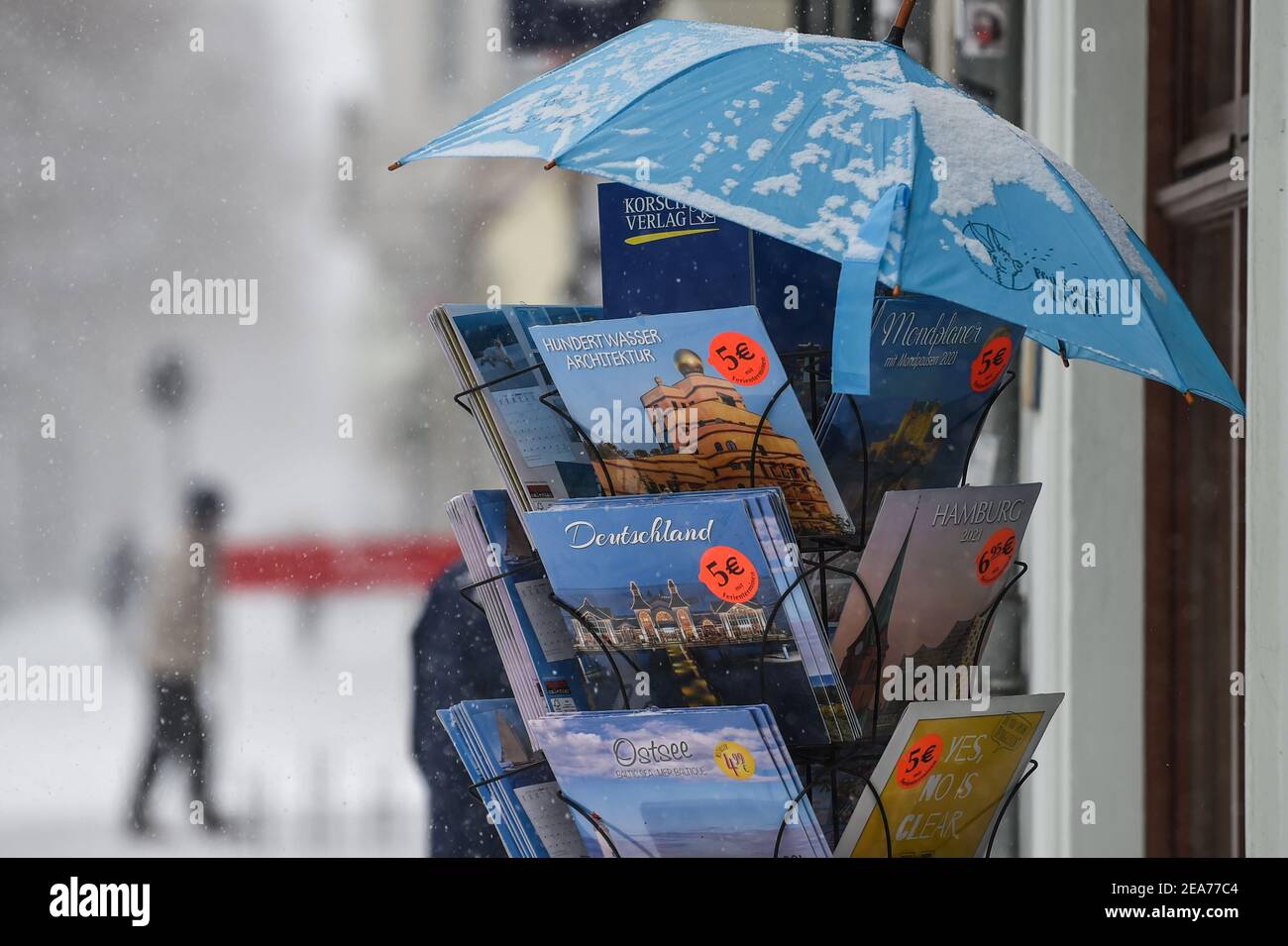 Berlin, Deutschland. Februar 2021, 08th. In einer Buchhandlung in der Bölschestraße Friedrichshagen gibt es einen Stand mit Büchern und Kalendern, die durch einen Regenschirm vor dem Schnee geschützt sind. Quelle: Kira Hofmann/dpa-Zentralbild/dpa/Alamy Live News Stockfoto