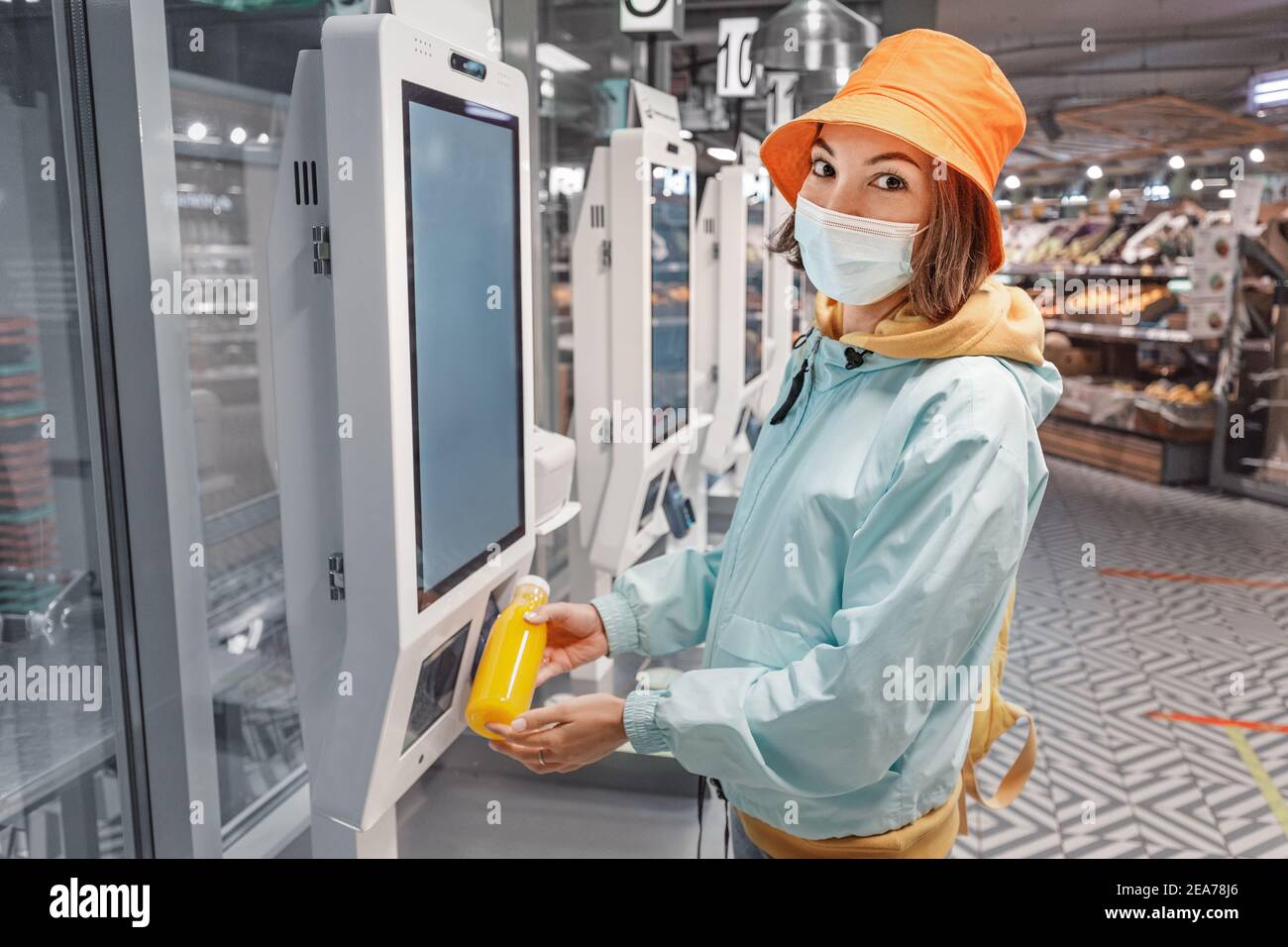 Eine Frau in einer medizinischen Schutzmaske kauft eine Flasche frischen Saft an einer Selbstbedienungskasse in einem Supermarkt. Das Konzept der Coronavirus-Ökonomie Stockfoto