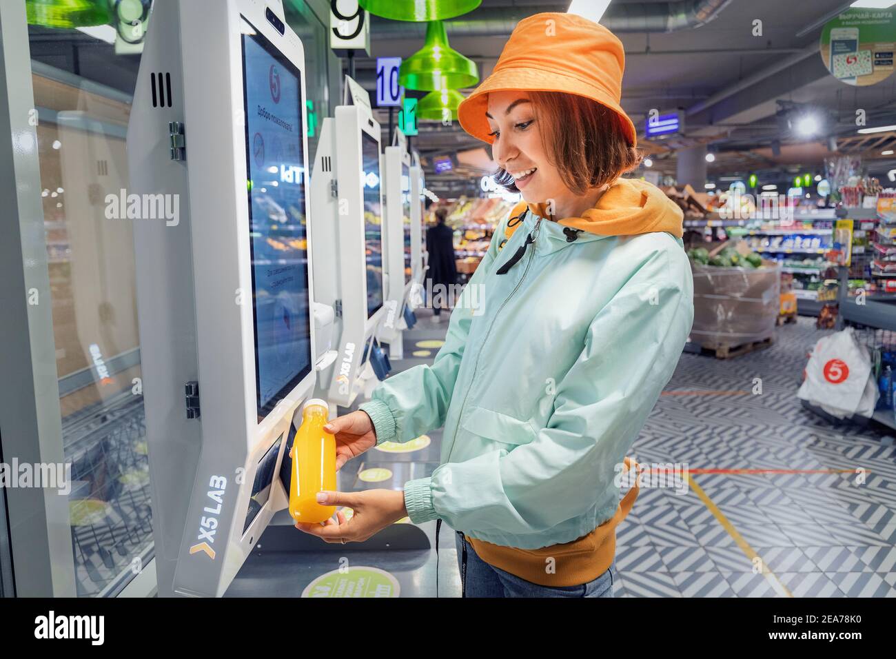 02. September 2020, Moskau, Russland: Glückliche junge Kundin Frau kauft und zahlt für eine Flasche Orangensaft an der Kasse eines Self-Service-Maschine in Stockfoto