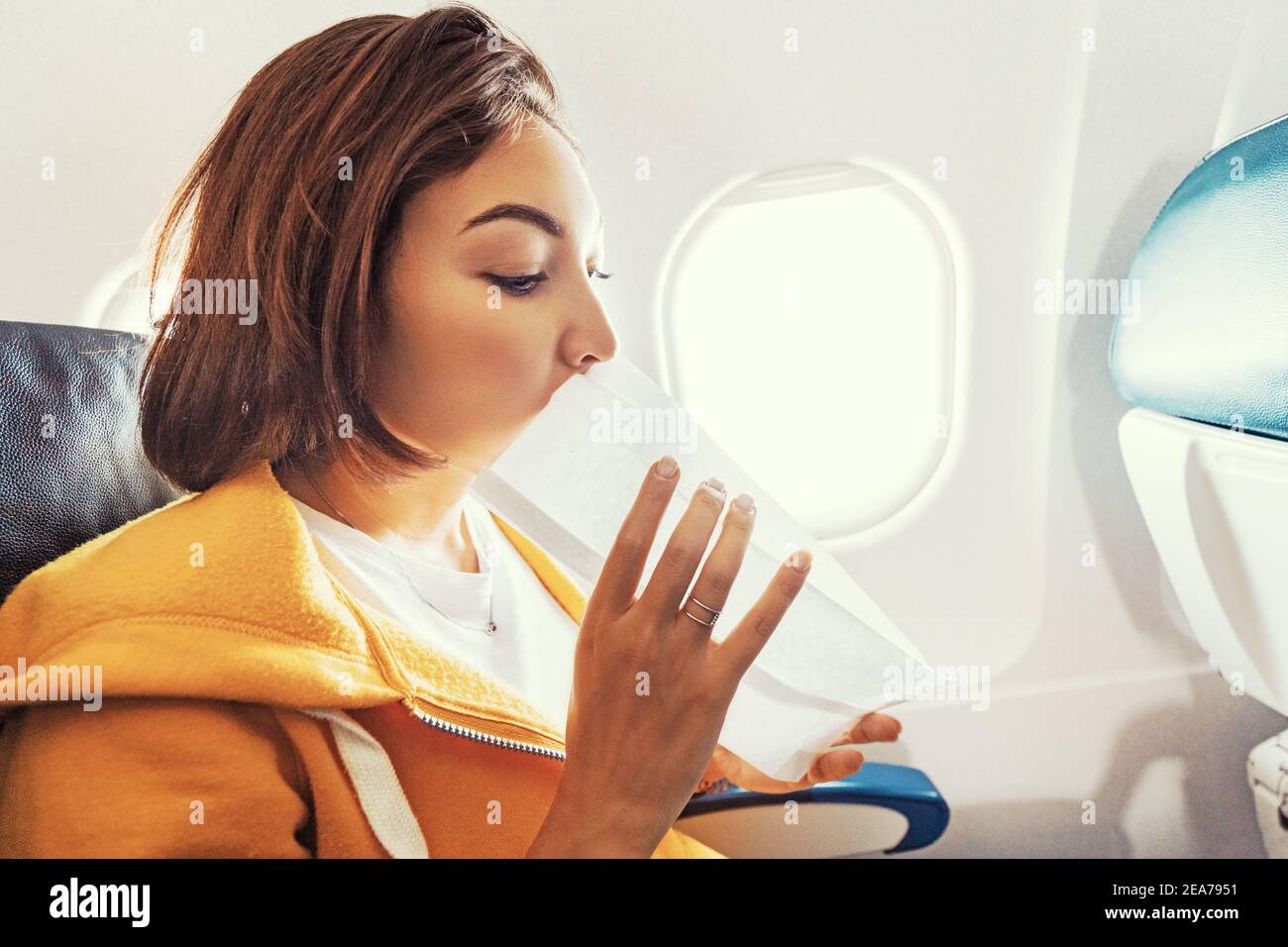 Eine asiatische weibliche Reisende leidet unter einem akuten Angriff von Übelkeit während Turbulenzen auf einem Flugzeug. Die Frau war seekrank und Luftsocke während des Flugs Stockfoto